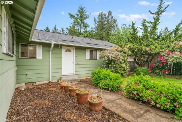 doorway to property with roof with shingles and fence