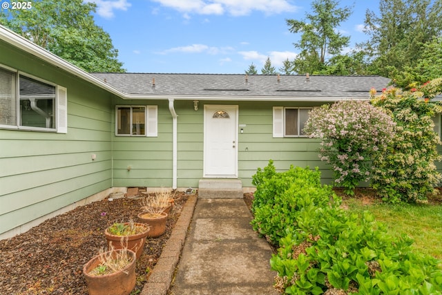 view of exterior entry with roof with shingles