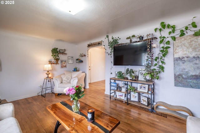 living room with baseboards, arched walkways, a textured ceiling, and hardwood / wood-style floors