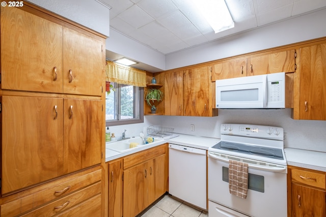 kitchen with a sink, white appliances, light tile patterned flooring, brown cabinetry, and light countertops