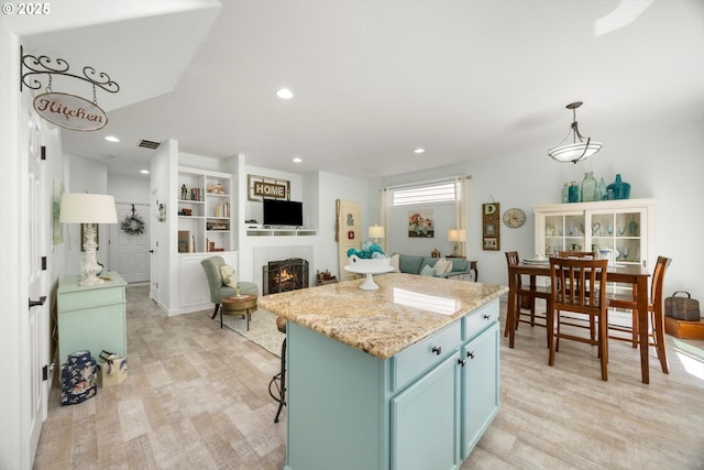 19774 SW Ashcroft Ln, Beaverton, OR 97003 - kitchen with blue cabinets, light wood-type flooring, a warm lit fireplace, a kitchen island, and recessed lighting