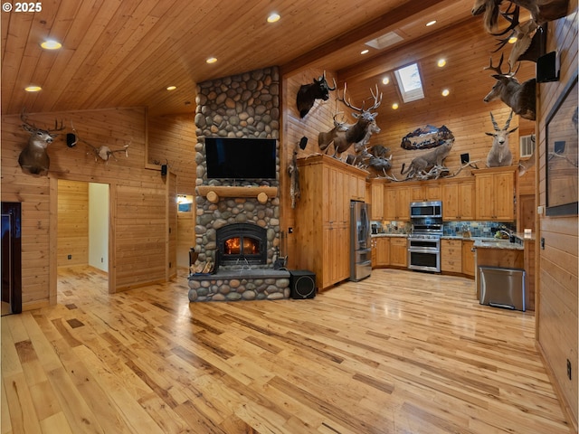 kitchen featuring wooden walls, stainless steel appliances, a stone fireplace, and open floor plan