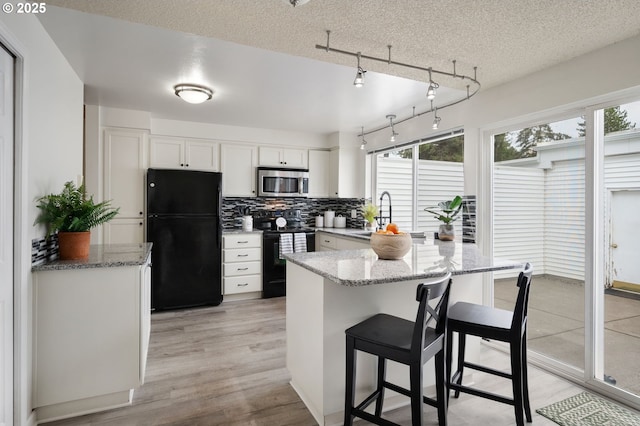 kitchen with white cabinetry, decorative backsplash, light stone countertops, black appliances, and sink