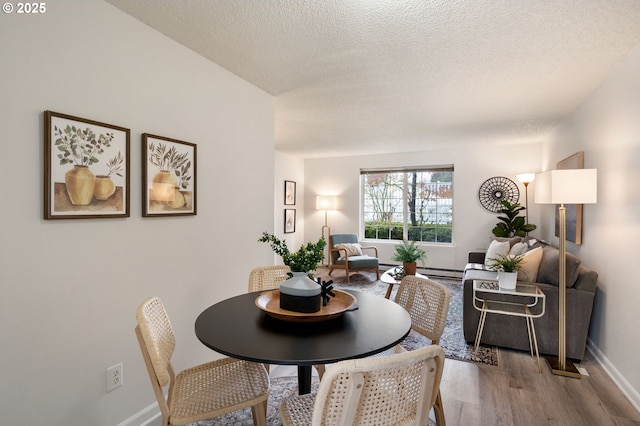 dining space with a textured ceiling, baseboard heating, and wood-type flooring