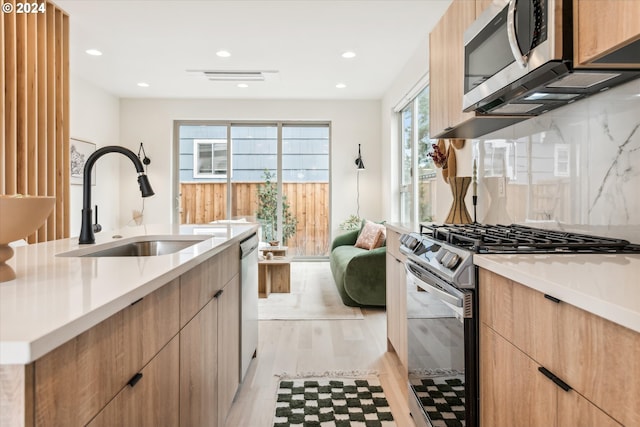 kitchen with sink, appliances with stainless steel finishes, tasteful backsplash, light brown cabinets, and light wood-type flooring