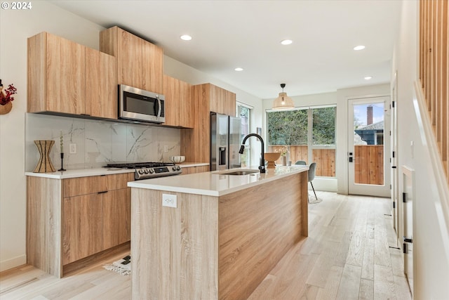 kitchen featuring a wealth of natural light, sink, a kitchen island with sink, stainless steel appliances, and light wood-type flooring