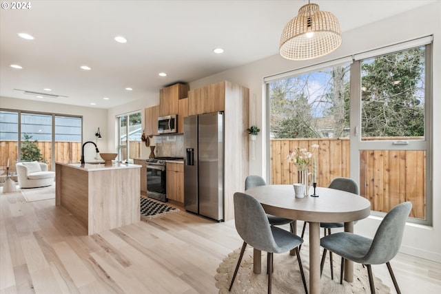 kitchen with pendant lighting, light hardwood / wood-style flooring, a kitchen island with sink, stainless steel appliances, and decorative backsplash