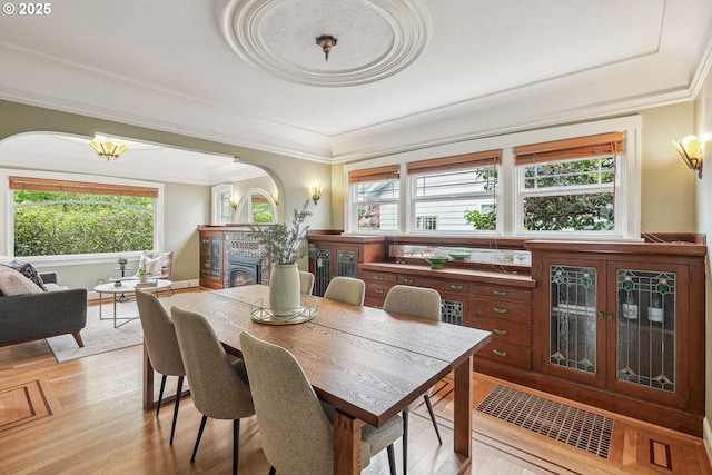 dining room with crown molding, arched walkways, a lit fireplace, and a healthy amount of sunlight
