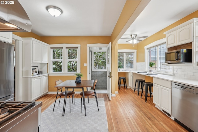 kitchen featuring appliances with stainless steel finishes, decorative backsplash, light wood-style flooring, and white cabinetry