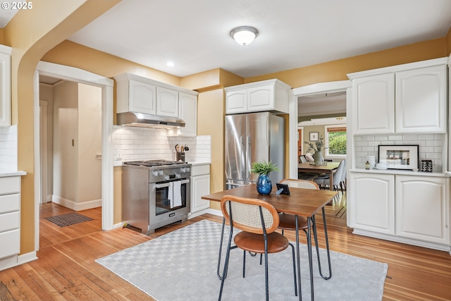 kitchen with decorative backsplash, light wood finished floors, under cabinet range hood, stainless steel appliances, and white cabinetry