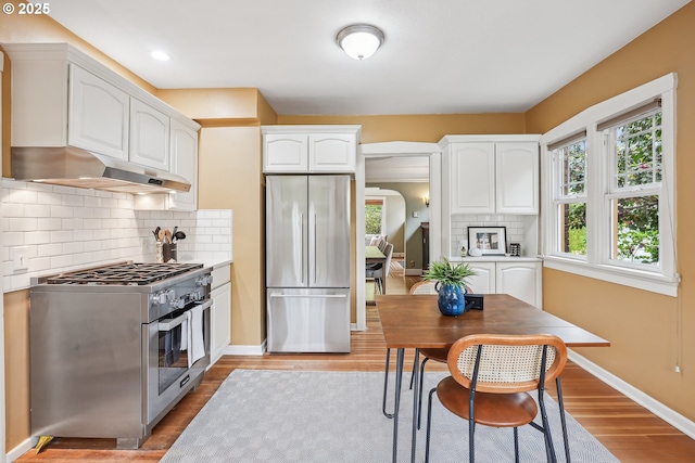 kitchen featuring decorative backsplash, white cabinetry, under cabinet range hood, light wood finished floors, and appliances with stainless steel finishes