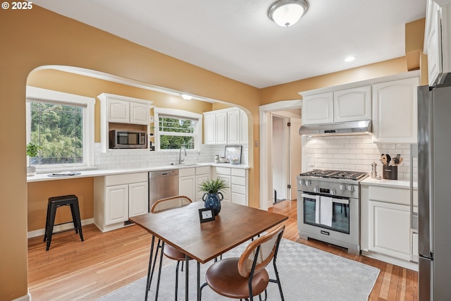 kitchen with decorative backsplash, appliances with stainless steel finishes, a sink, under cabinet range hood, and white cabinetry