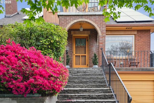 doorway to property with brick siding and roof mounted solar panels