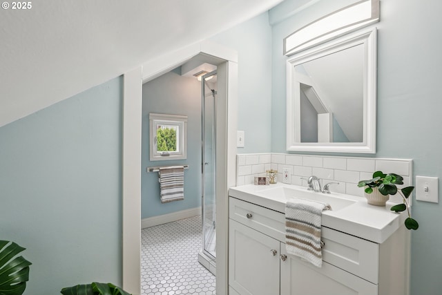 bathroom featuring vanity, baseboards, lofted ceiling, tasteful backsplash, and a stall shower