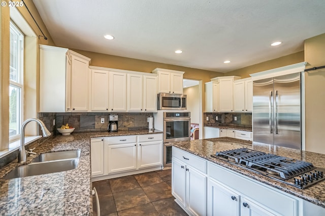 kitchen with stainless steel appliances, a sink, backsplash, white cabinetry, and recessed lighting