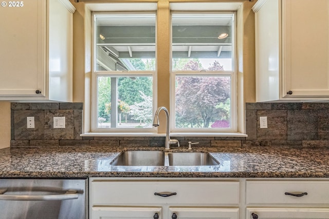 kitchen with stainless steel dishwasher, a sink, dark stone countertops, white cabinets, and decorative backsplash