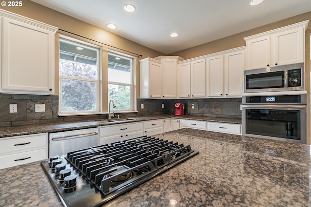 kitchen with appliances with stainless steel finishes, a sink, white cabinetry, recessed lighting, and dark stone countertops