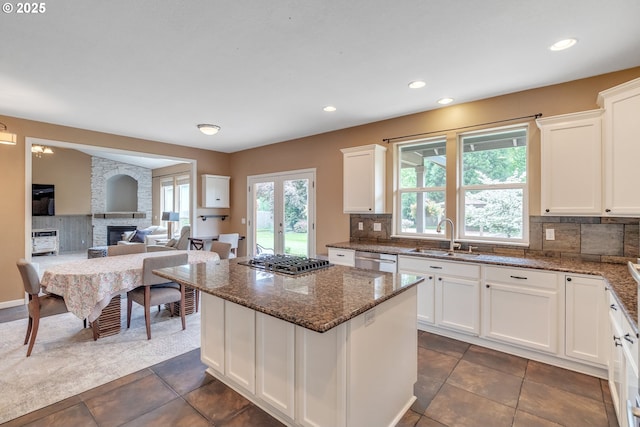 kitchen with a sink, stainless steel appliances, tasteful backsplash, white cabinets, and a fireplace