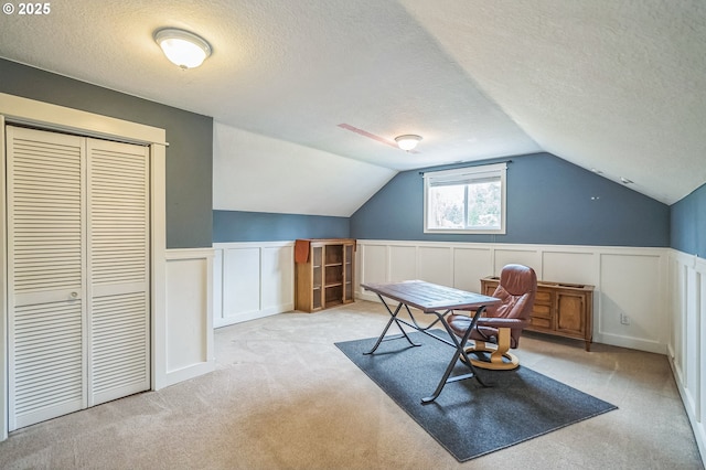 carpeted office with a textured ceiling, a decorative wall, lofted ceiling, and wainscoting