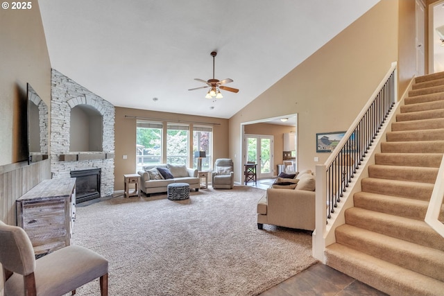 living room with a ceiling fan, a stone fireplace, stairway, high vaulted ceiling, and carpet