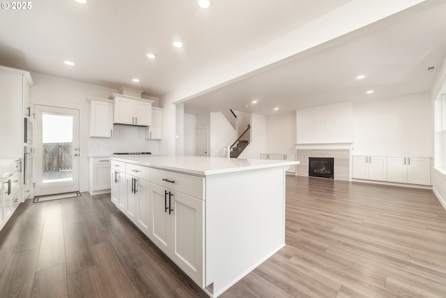 kitchen featuring white cabinetry, a center island, light hardwood / wood-style flooring, white appliances, and decorative backsplash