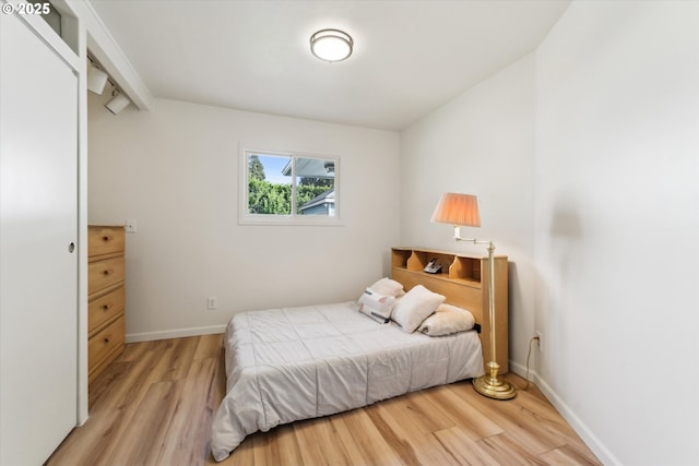 bedroom featuring light wood-type flooring, baseboards, and beamed ceiling