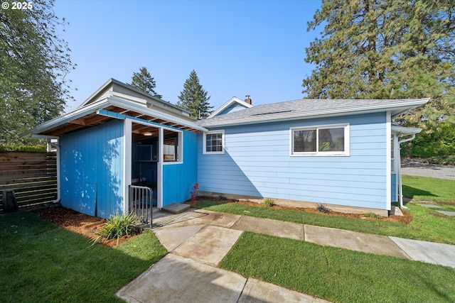 view of front of property featuring an outbuilding, fence, roof with shingles, a chimney, and a front yard