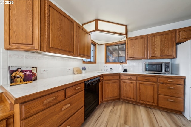 kitchen featuring black dishwasher, stainless steel microwave, backsplash, brown cabinetry, and a sink