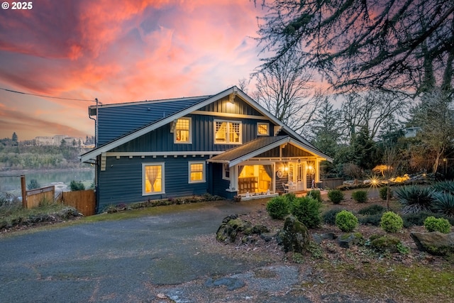 back of house at dusk featuring covered porch, driveway, board and batten siding, and fence