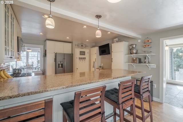 kitchen featuring white cabinetry, plenty of natural light, stainless steel refrigerator with ice dispenser, and a peninsula