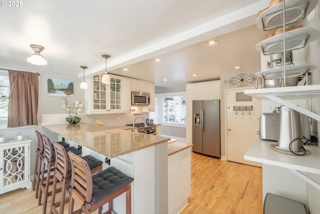 kitchen featuring appliances with stainless steel finishes, glass insert cabinets, white cabinets, light wood-type flooring, and a peninsula