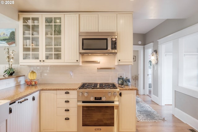 kitchen featuring light stone countertops, glass insert cabinets, stainless steel appliances, and decorative backsplash