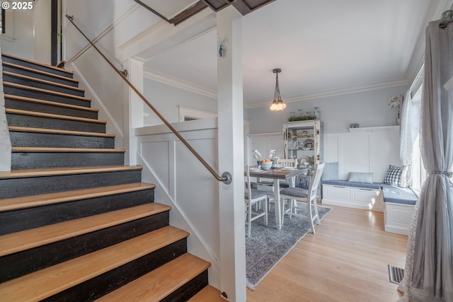 stairs featuring a decorative wall, wood finished floors, visible vents, and crown molding