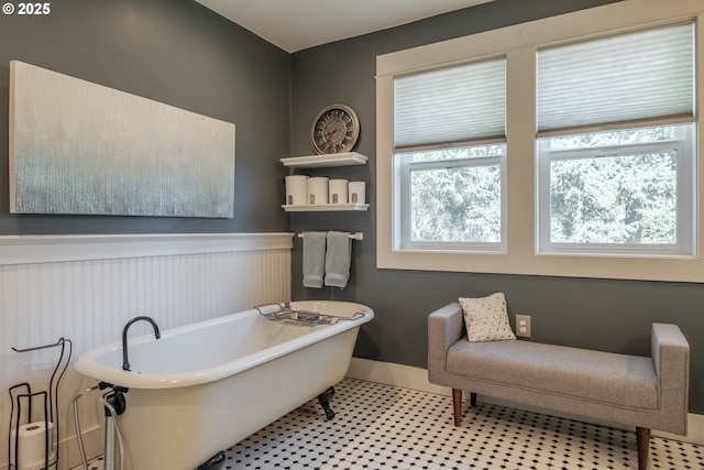 bathroom featuring a wainscoted wall, a soaking tub, and baseboards