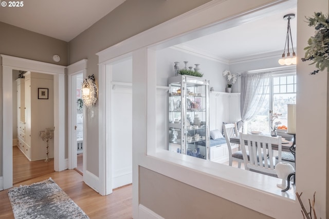 hallway featuring light wood finished floors, baseboards, and crown molding