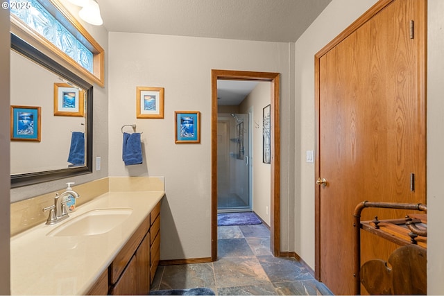 full bathroom with stone tile flooring, a shower stall, baseboards, and vanity
