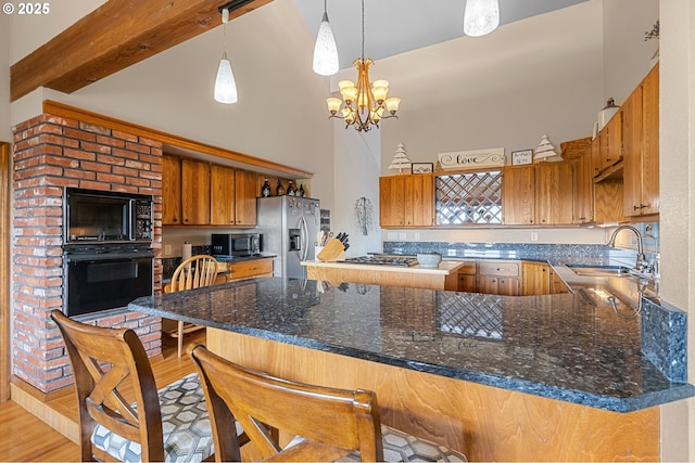 kitchen with a sink, black appliances, brown cabinets, a peninsula, and a high ceiling