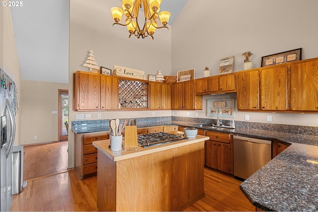 kitchen featuring stainless steel appliances, light wood-style flooring, a sink, a notable chandelier, and high vaulted ceiling