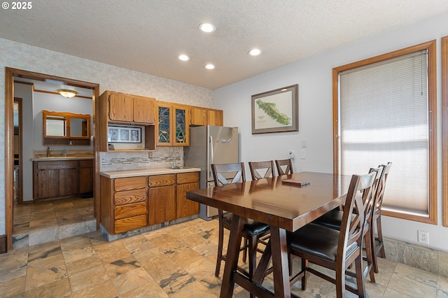 kitchen with brown cabinetry, a sink, a textured ceiling, and stainless steel appliances