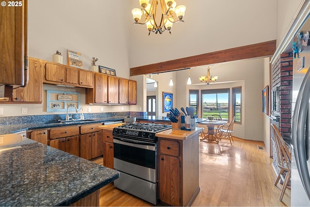 kitchen with brown cabinets, a towering ceiling, a sink, stainless steel gas range, and a chandelier