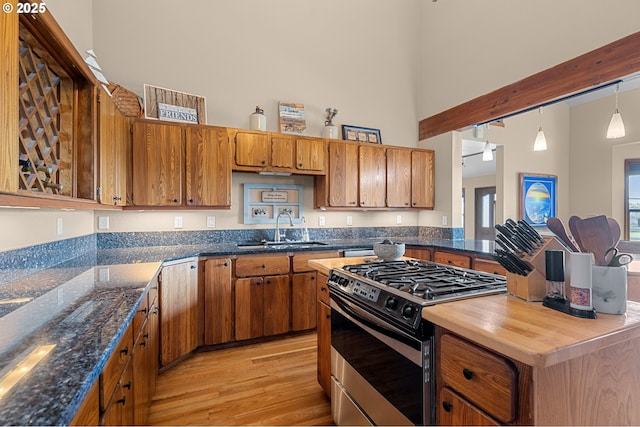 kitchen with light wood-style flooring, a sink, a towering ceiling, brown cabinets, and stainless steel gas range oven