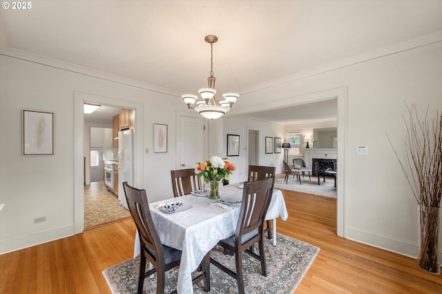 dining room with a chandelier, light wood finished floors, baseboards, and ornamental molding