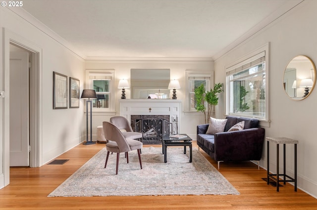 living area with ornamental molding, a fireplace, baseboards, and wood finished floors