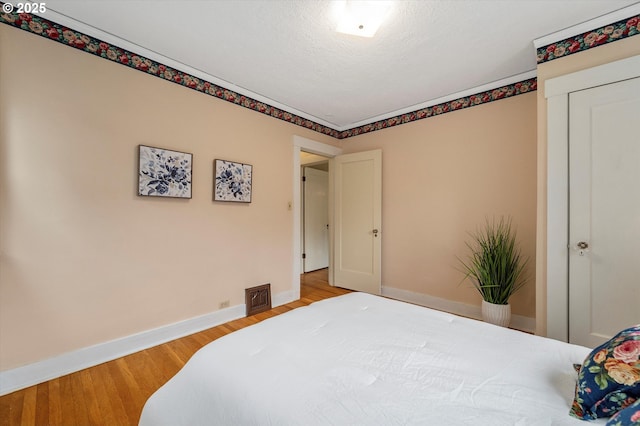 bedroom featuring visible vents, light wood-style flooring, a textured ceiling, and baseboards