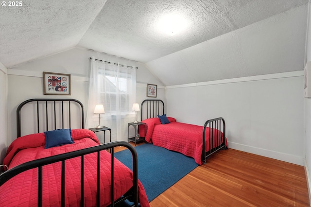 bedroom with vaulted ceiling, a textured ceiling, baseboards, and wood finished floors