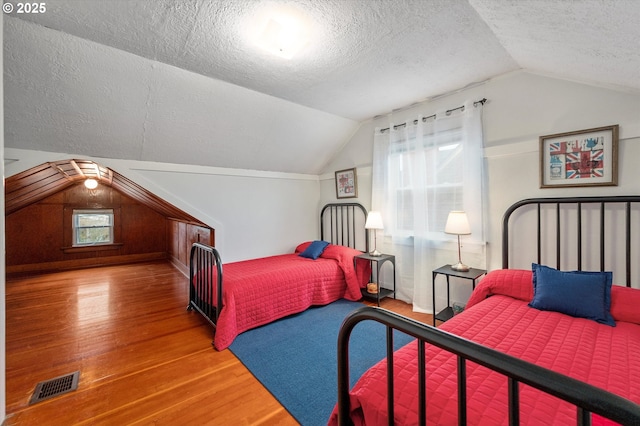 bedroom with visible vents, a textured ceiling, lofted ceiling, and wood finished floors