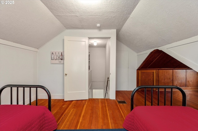 bedroom featuring vaulted ceiling, visible vents, a textured ceiling, and wood finished floors