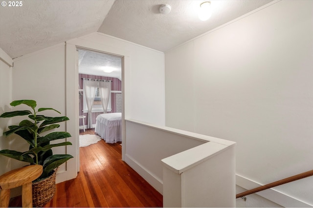 hall featuring vaulted ceiling, an upstairs landing, wood-type flooring, and a textured ceiling