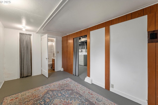 bedroom with washer / clothes dryer, ensuite bath, finished concrete flooring, and wood walls