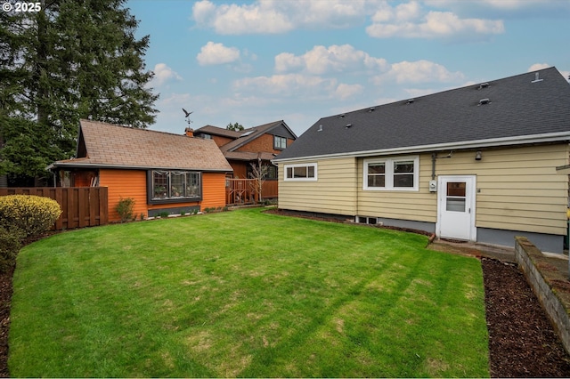 back of property with roof with shingles, a yard, and fence